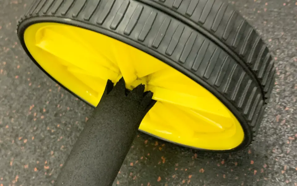 Close-up of a yellow and black ab roller wheel on a gym floor